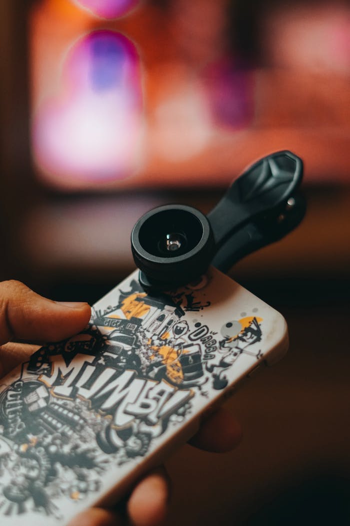 services-02 Smartphone with clip-on lens held in hand, capturing close-up shots indoors.